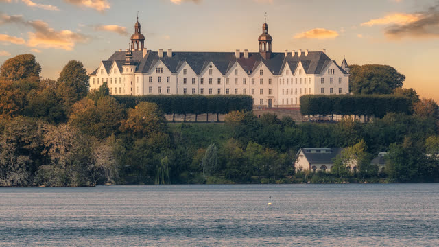Das weiße Schloss Plön auf dem Hügel über dem Plöner See im Abendlicht